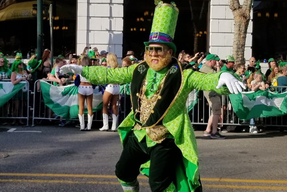 A man dressed up as a leprechaun in green and black with shamrocks during a street parade.