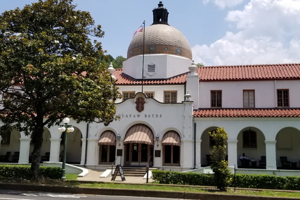A white stucco building with brown awnings and a tiled roof with the name Ouapaw Baths over the main entrance.