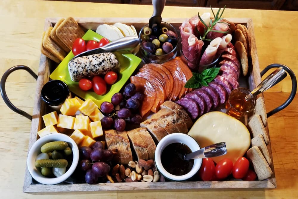 A tray full of various cheeses, meats, fresh fruits, and crackers.