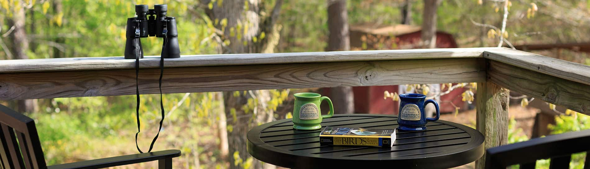 Black deck table with coffee cups and a book, next to the deck railing with binoculars