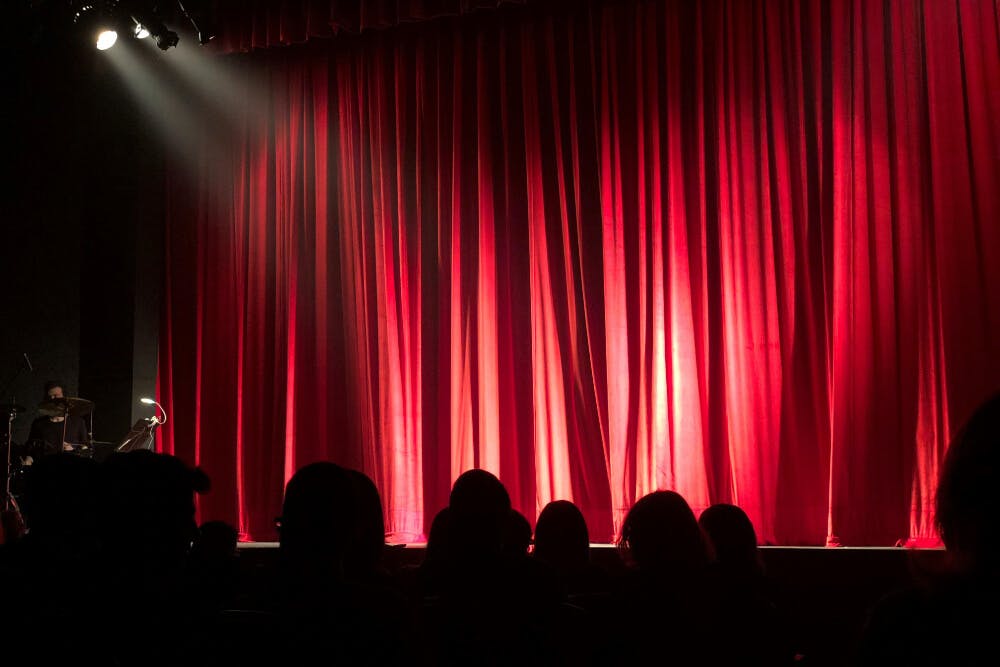 Some people in a dark theater in front of a red curtain waiting for a performance.