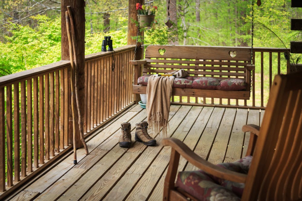 A porch with wood floors and railings, a wood porch swing, and wooden rocking chairs.
