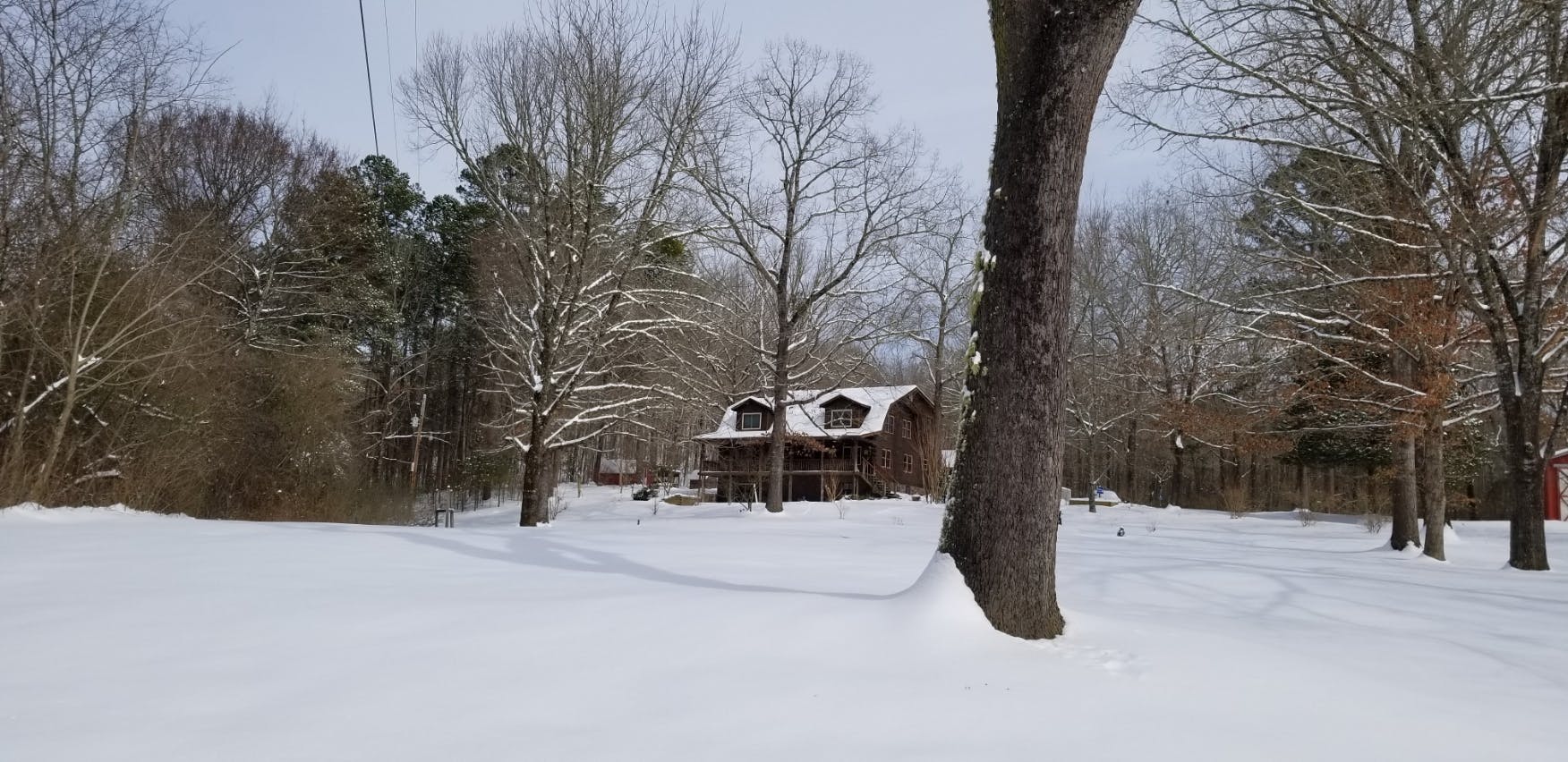 A large yard coverd in snow with a log house in the background, also covered in snow