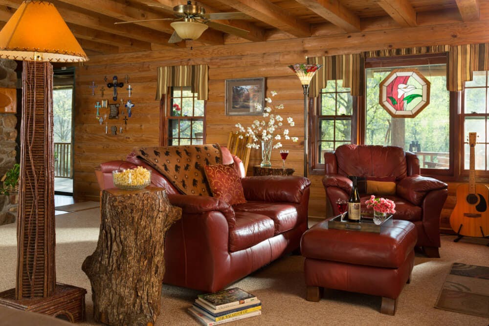 A welcoming living room in a log house with red leather furniture, wood accent furnishings, and a stained glass in the window.