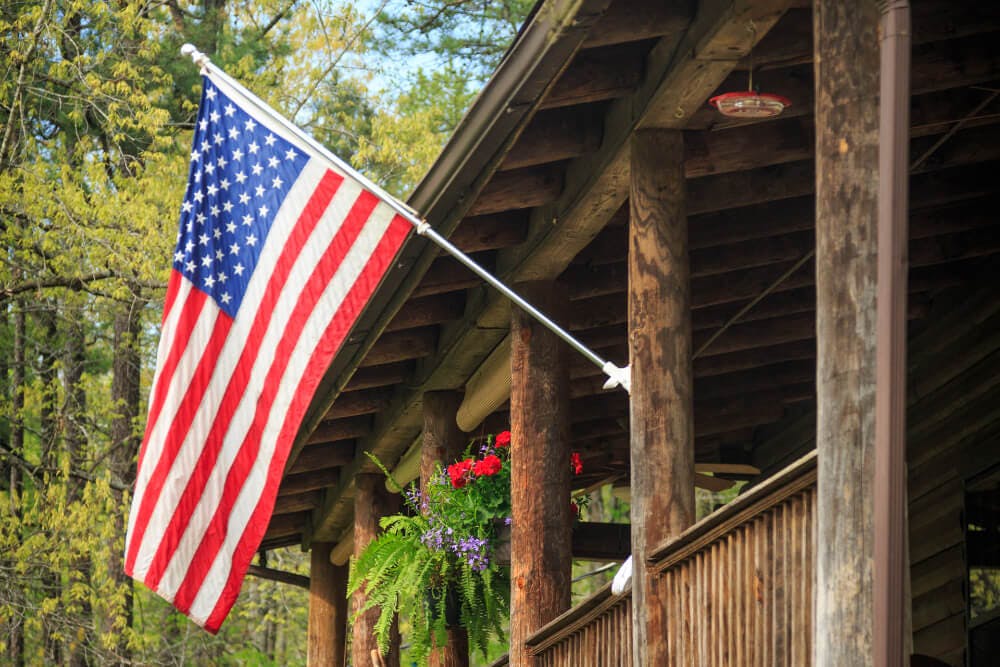 A wood log porch with an American flag hanging at the front of the porch.
