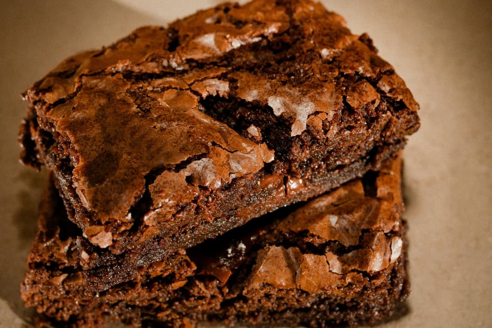 Two brownies cut in squares and stacked on top of eachother on an off-white plate.